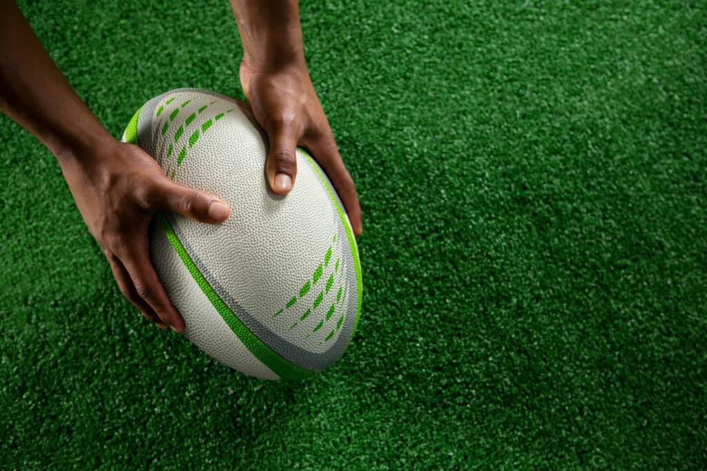 hands holding rugby ball on field