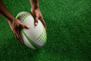 hands holding rugby ball on field